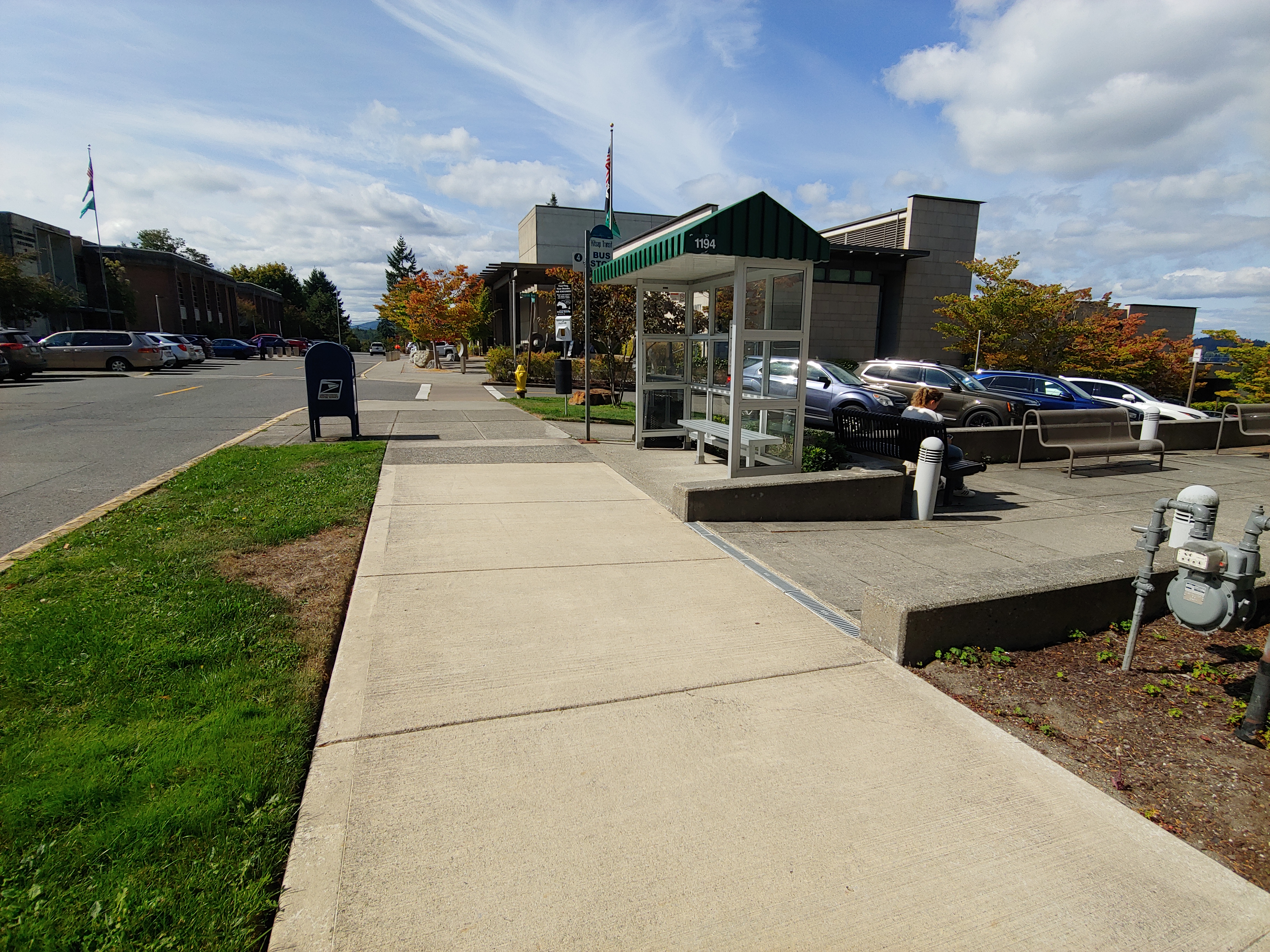 On the footpath leading across a road in front of a bus top. This picture is taken in front of the Kitsap County Public Works building on a sunny day.