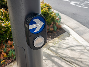 A cross walk pedestrian push button a a damp grey pole at a curb